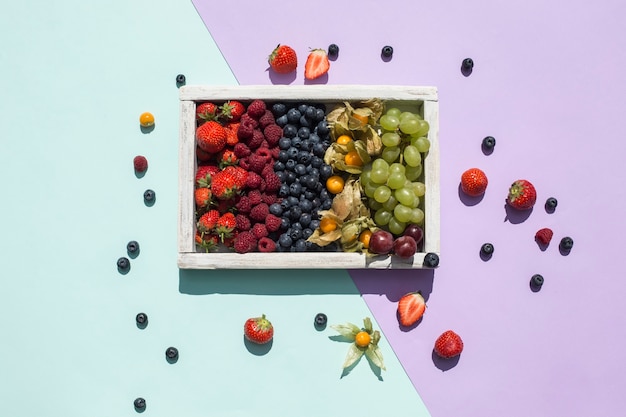 Photo un mélange de baies fraîches dans une boîte en bois sur un fond vert et violet vif. les tropiques. alimentation saine pour un régime. vitamines. vue de dessus avec un espace de copie. orientation horizontale.