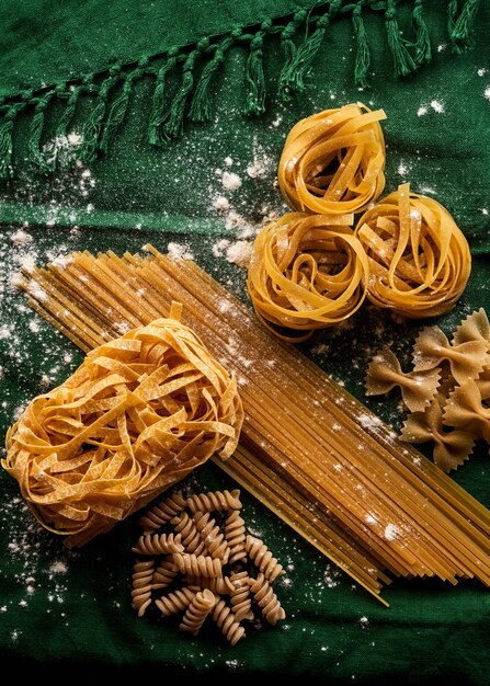 Mélange de différentes variétés de pâtes sur fond de tissu vert, concept de macaroni assorti de cuisson