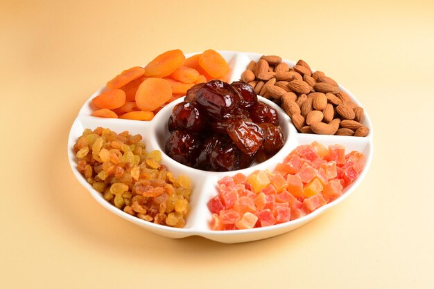 Mélange de fruits secs et de noix sur une assiette blanche. Abricot, amande, raisin sec, dattes fruits. Sur fond beige. Espace pour le texte ou la conception.