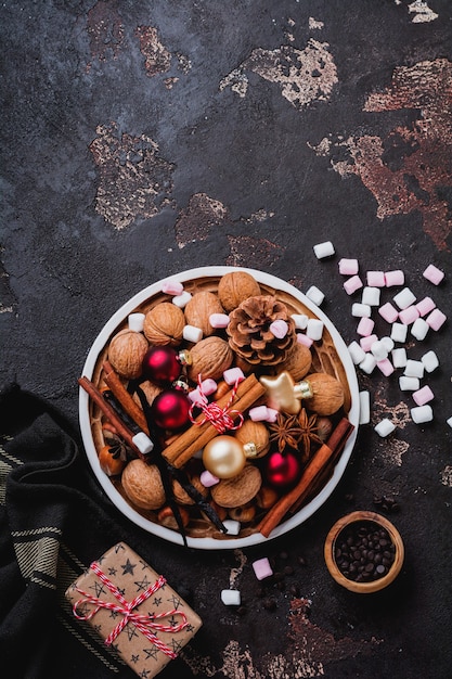 Mélange de noisettes et de noix crues saines, bâtons de cannelle, anis, vanille, chocolat et jouets de Noël dans une plaque en céramique sur une surface en béton brun