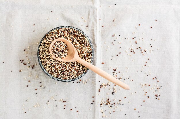 Mélange de quinoa cru blanc rouge et noir et une cuillère en bois dans un bol sur un chiffon Nourriture saine sans gluten Vue de dessus