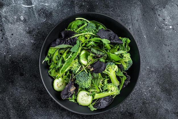 Mélange de salade fraîche d'épinards, de feuilles de roquette, de blettes et de mâche avec légumes. Fond noir. Vue de dessus.