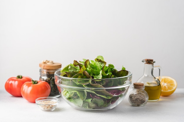 Mélange de salade verte dans un bol en verre avec des tomates, de l'huile et plus encore sur la table sur fond gris clair