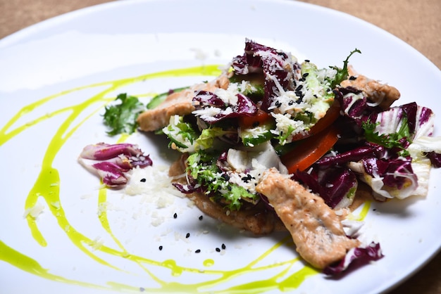 Mélange de salades et de volaille sur une assiette blanche avec de l'huile d'olive Concept d'entrée ou de repas diététique Salade de laitue verte au chou violet et de poulet sur fond beige Apéritif servi au restaurant