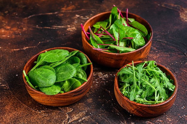 Mélanger les feuilles de salade, la roquette, les épinards et la bette à carde dans des bols en bois. Fond sombre. Vue de dessus.