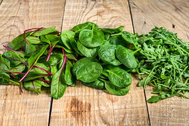 Mélanger les feuilles de salade, la roquette, les épinards et les blettes. Fond en bois. Vue de dessus.