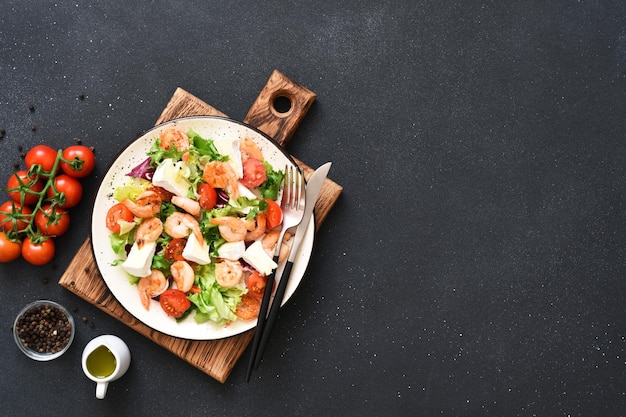 Mélanger la salade avec du fromage brie aux crevettes et de la sauce tomate sur une vue de dessus de fond en béton noir