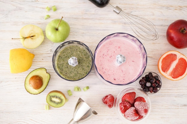 Mélangeur à main électrique en plastique et accessoires avec fruits sur fond bois, plat.