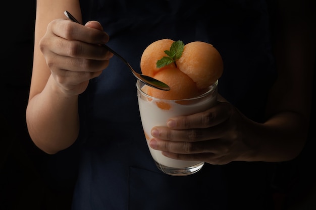 Photo melon à chair jaune a été versé dans une boule ronde comme de la crème glacée. mettre dans un verre transparent garni de lait frais, sucré et délicieux. prenez une photo sur fond noir