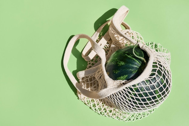 Photo melon d'eau dans un sac de shopping en maille réutilisable de désintoxication fruit exotique sur fond vert pastel