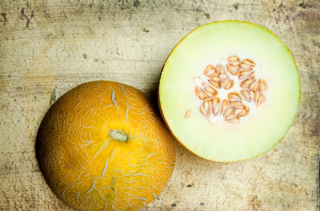 Melon jaune doux moitié coupé sur une table rustique doré.