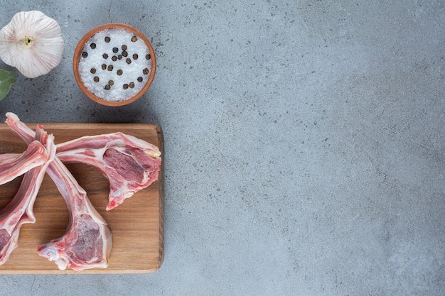 Membres d'agneau crus avec du sel et de l'ail sur planche de bois.