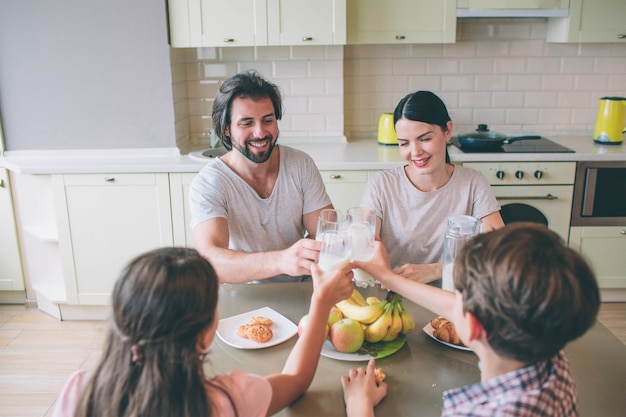 Les membres d'une famille sont assis à table et tiennent ensemble des verres de lait. Ils sourient. La famille prend le petit déjeuner.