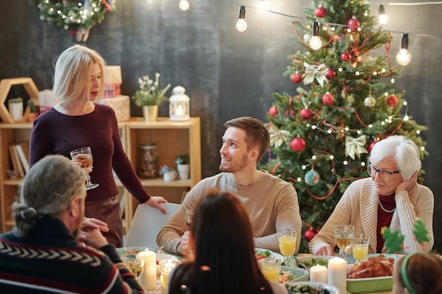 Les membres de la grande famille à la femme blonde mature avec un verre de vin faisant des toasts de Noël par dîner de fête