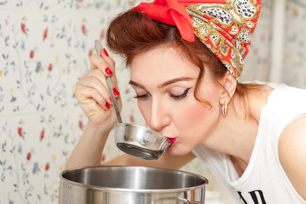 Ménagère gaie dans un foulard rouge dans la cuisine tente la soupe