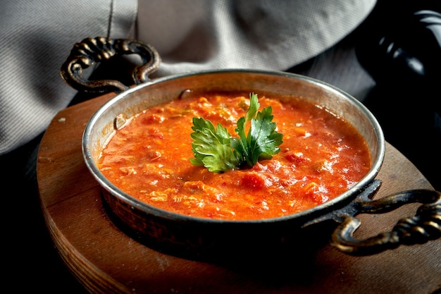 Menemen - petit-déjeuner turc populaire qui comprend des œufs, des tomates, des poivrons verts et des épices dans une casserole en cuivre sur fond noir