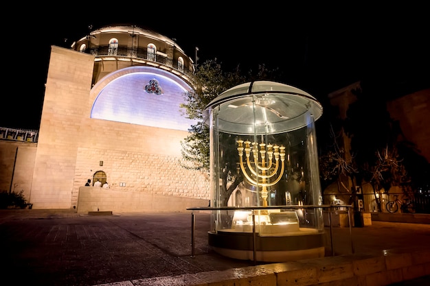 Menorah - la lampe dorée à sept barils - l'emblème juif national et religieux près des portes Dung sur le fond de la synagogue Hurva la nuit dans la vieille ville de Jérusalem, Israël.