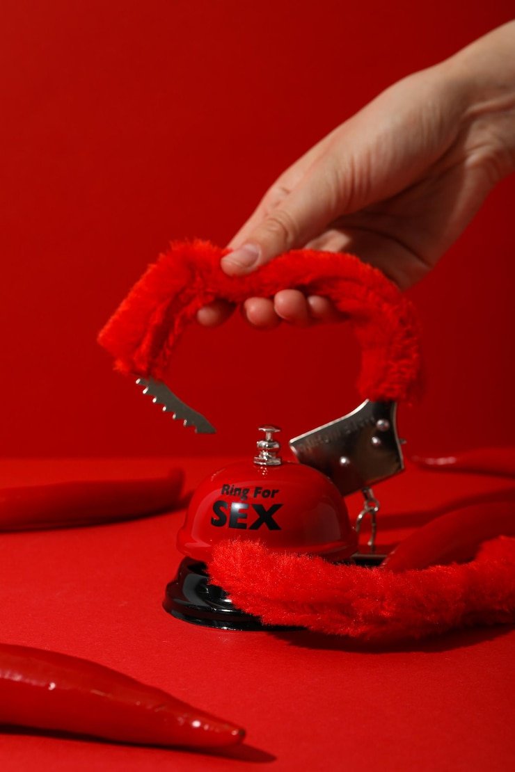 Photo menottes et une cloche pour le sexe avec du poivre sur fond rouge