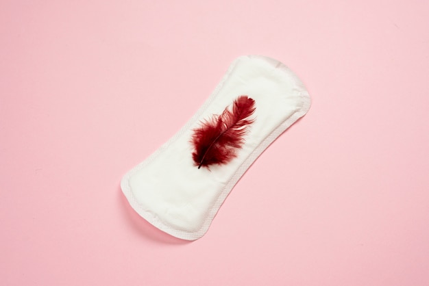 Menstruation. Femme blanche couchée. Doublure féminine avec plume rouge. Journées critiques des femmes.