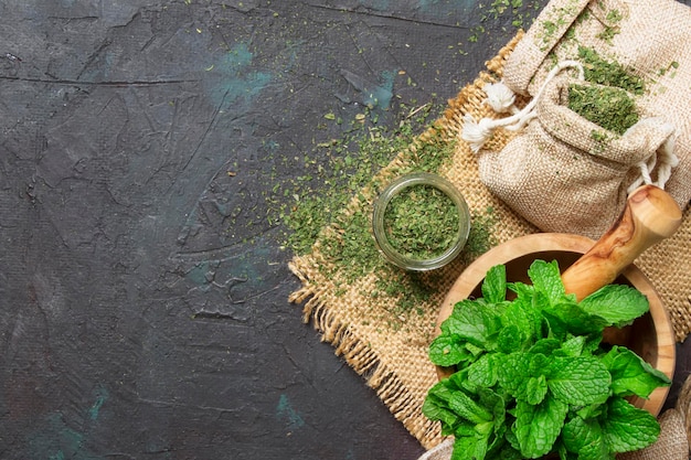 Menthe poivrée séchée dans un bocal en verre et un tas d'herbe médicinale à la menthe fraîche sur fond noir vue de dessus