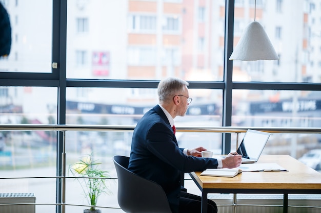 Mentor masculin adulte, réalisateur, homme d'affaires à lunettes et un costume étudiant des documents tout en étant assis à la table. Notion de jour ouvrable