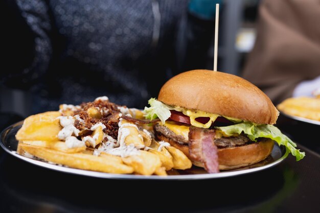 Menu combo en gros plan avec hamburger gastronomique et frites avec sauce sur table. Femme méconnaissable sur fond