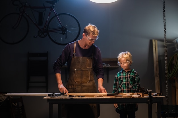 Photo un menuisier expérimenté montre le travail de divers outils à son fils dans l'atelier.