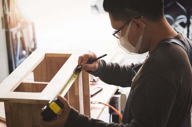 Un menuisier mesure les planches pour assembler les pièces et construire une table en bois pour le client