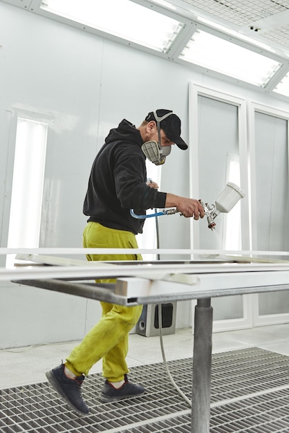 Le menuisier peint les détails des meubles en blanc dans l'atelier de menuiserie Plan vertical Vue latérale