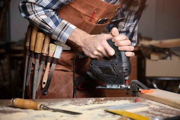 Le menuisier scie une planche de bois avec une scie sauteuse électrique dans l'atelier de menuiserie Workwood DIY concept Photographie de haute qualité