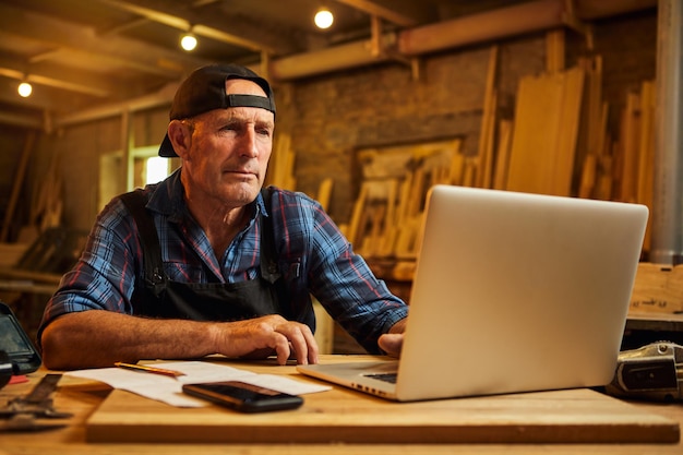 Le menuisier supérieur travaille sur l'ordinateur dans l'atelier