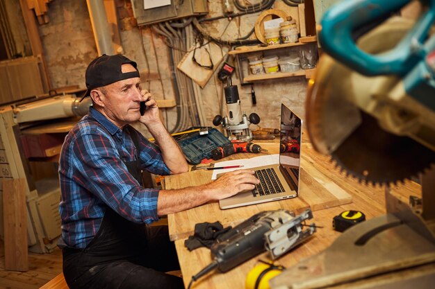 Le menuisier travaille sur l'ordinateur et parle au téléphone avec le client dans l'atelier