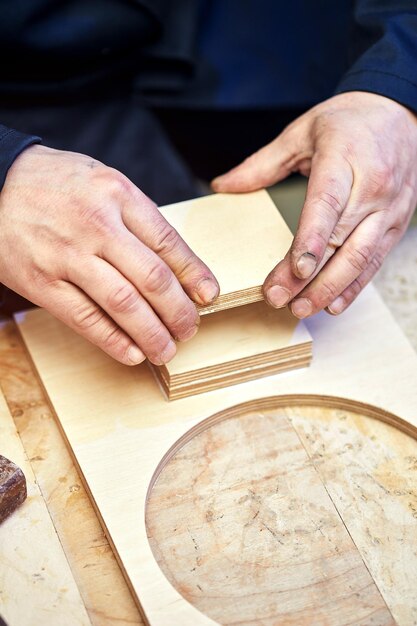 Le menuisier travaille avec des pièces en bois en collant des éléments de meulage dans l'atelier