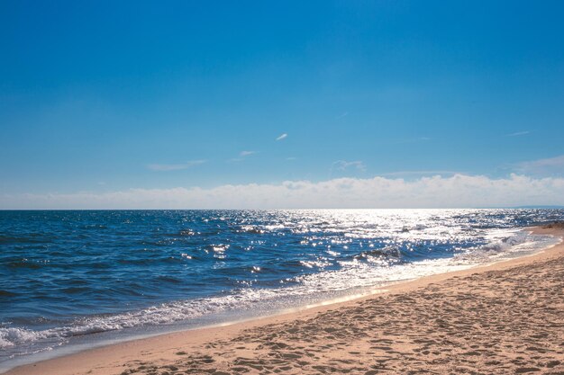 Mer bleue étincelante au soleil avec une plage de sable ondulée et un ciel bleu un jour d'été