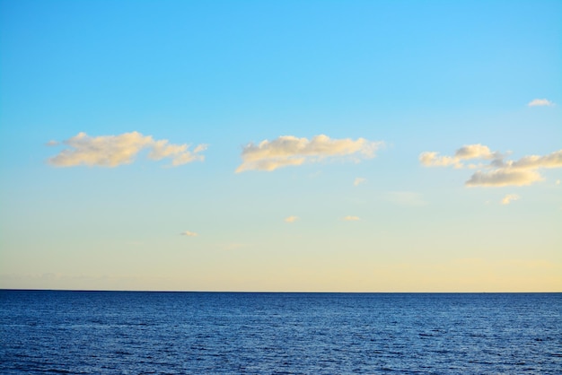 Mer bleue sous un ciel clair avec de petits nuages au coucher du soleil