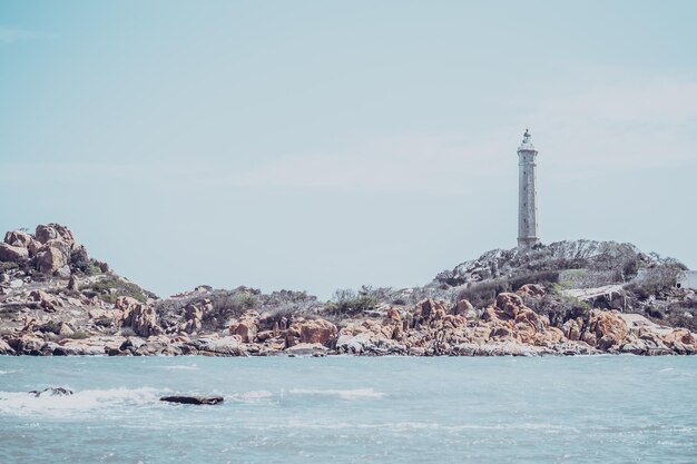 Mer nature vue panoramique paysage arrière-plan océan falaises rocheuses île boisée ciel bleu clair phare au sommet de la montagne signal avertir les marins naufrage concept de voyage espoir but de la vie