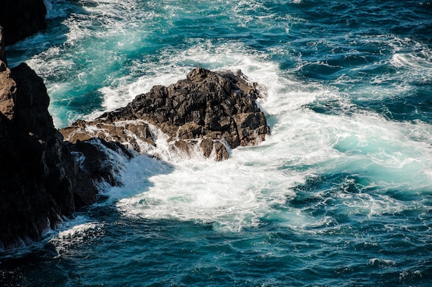 Mer profonde bleue et orageuse avec des vagues blanches et de la mousse autour du rocher aux beaux jours