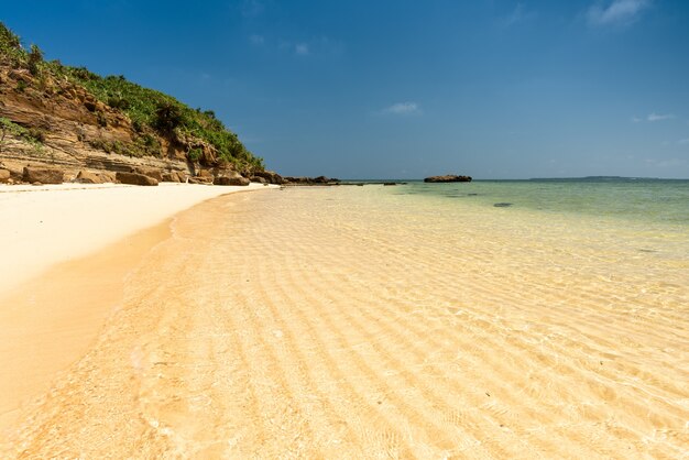 Mer transparente peu profonde sur un beau sable ondulé au bord de l'eau. Plage de falaise. L'île d'Iriomote.