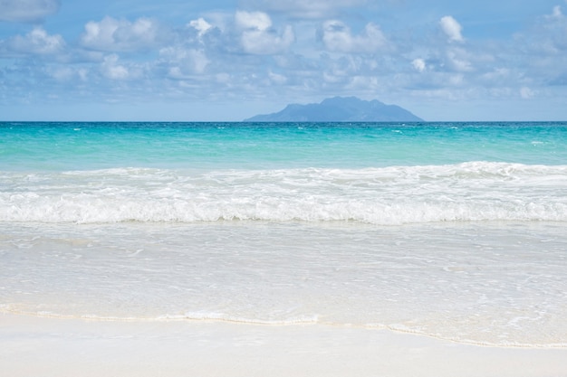 Mer tropicale d'été avec des vagues douces de sable de ciel bleu et une île lointaine solitaire, concept de vacances tropicales, espace de copie