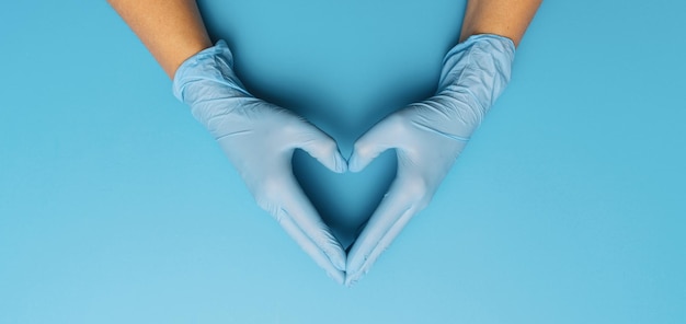 Merci aux médecins dans la pandémie de Corona, bannière horizontale avec espace de copie pour le texte. Les mains féminines dans des gants bleus montrent le symbole de la forme du coeur sur fond bleu.