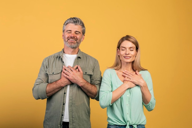 Merci Couple d'âge moyen reconnaissant avec les yeux fermés gardant les deux mains sur la poitrine exprimant la gratitude et la gentillesse