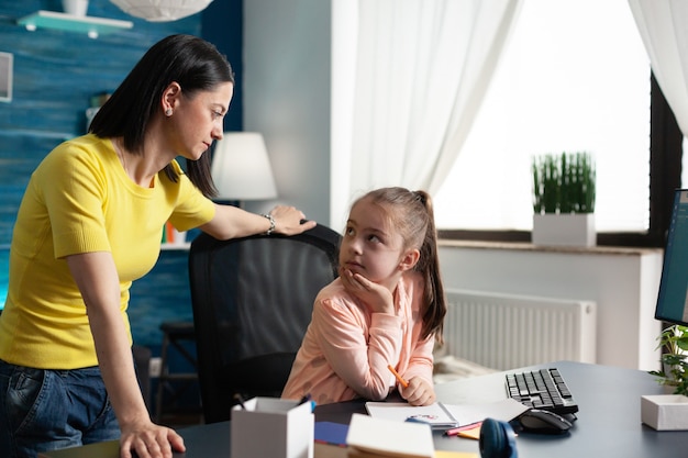 Mère adulte observant la petite fille faisant le travail scolaire