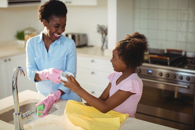 Mère aidant sa fille à nettoyer les ustensiles