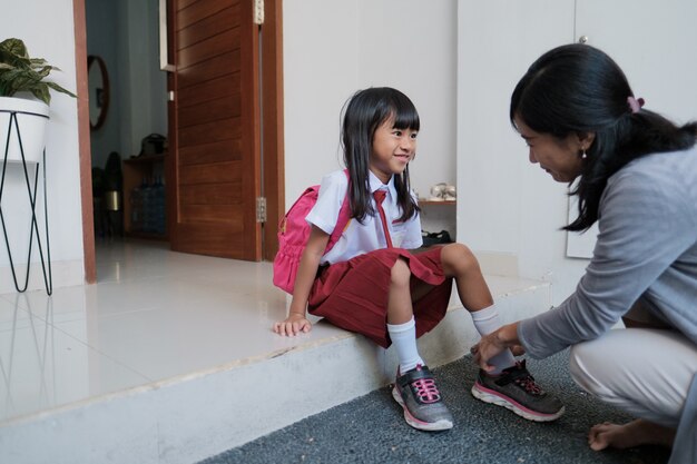 Une mère aide sa fille à porter des chaussures le matin en se préparant à aller à l'école