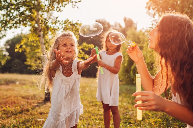 Une mère aide ses filles à souffler des bulles dans un parc d'été