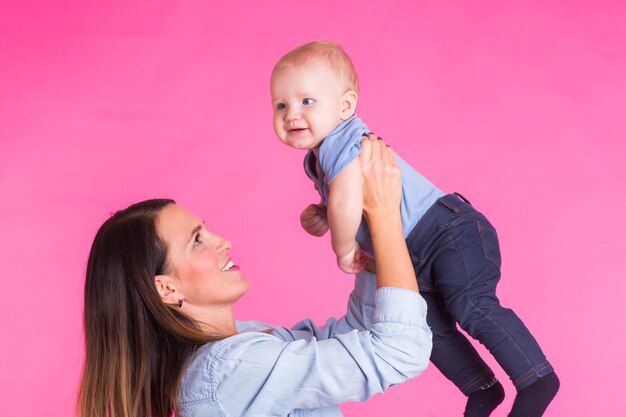 Mère aimante jouant avec son petit garçon sur un mur rose.