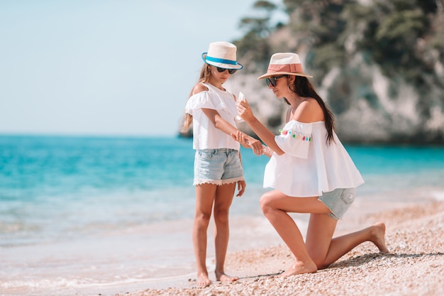 Mère appliquant une crème de protection solaire à sa fille sur une plage tropicale