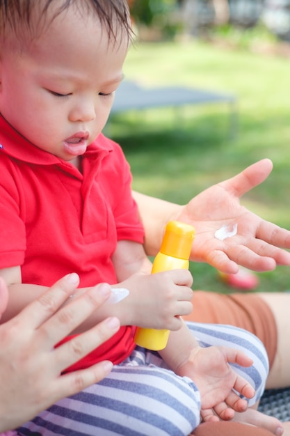 Mère d'appliquer la crème solaire sur mignon petit enfant asiatique