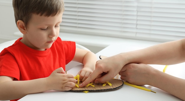 Mère apprenant à son fils à nouer des lacets de chaussures à l'aide d'un modèle en carton d'entraînement au gros plan d'une table blanche