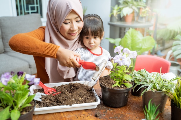 Une mère asiatique aide sa fille à tenir une petite pelle remplie de terre pour faire pousser des plantes en pot